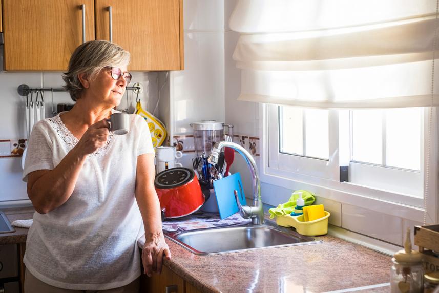 A senior looks out a kitchen window