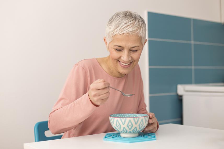 An older woman eats with a spoon and bowl