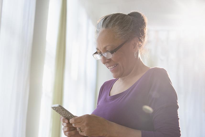 An elder standing by a window looks at a smartphone