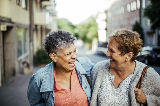 Two women walking on the street, smiling at each other and holding each other