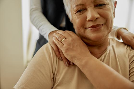 A seated elder person gets comfort from a hand on a shoulder